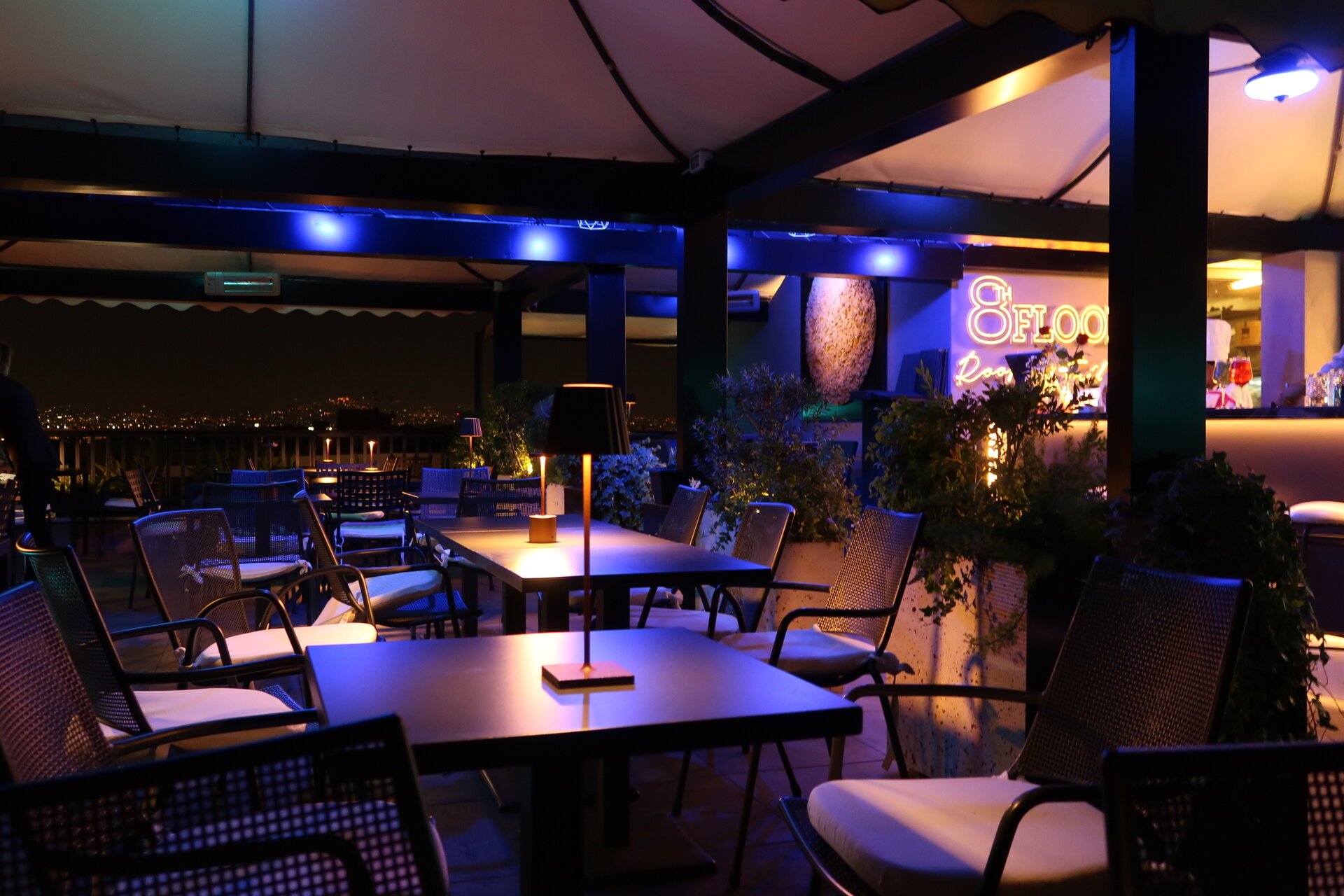 Atmosfera notturna del rooftop con tavoli illuminati e insegna 8 Floor